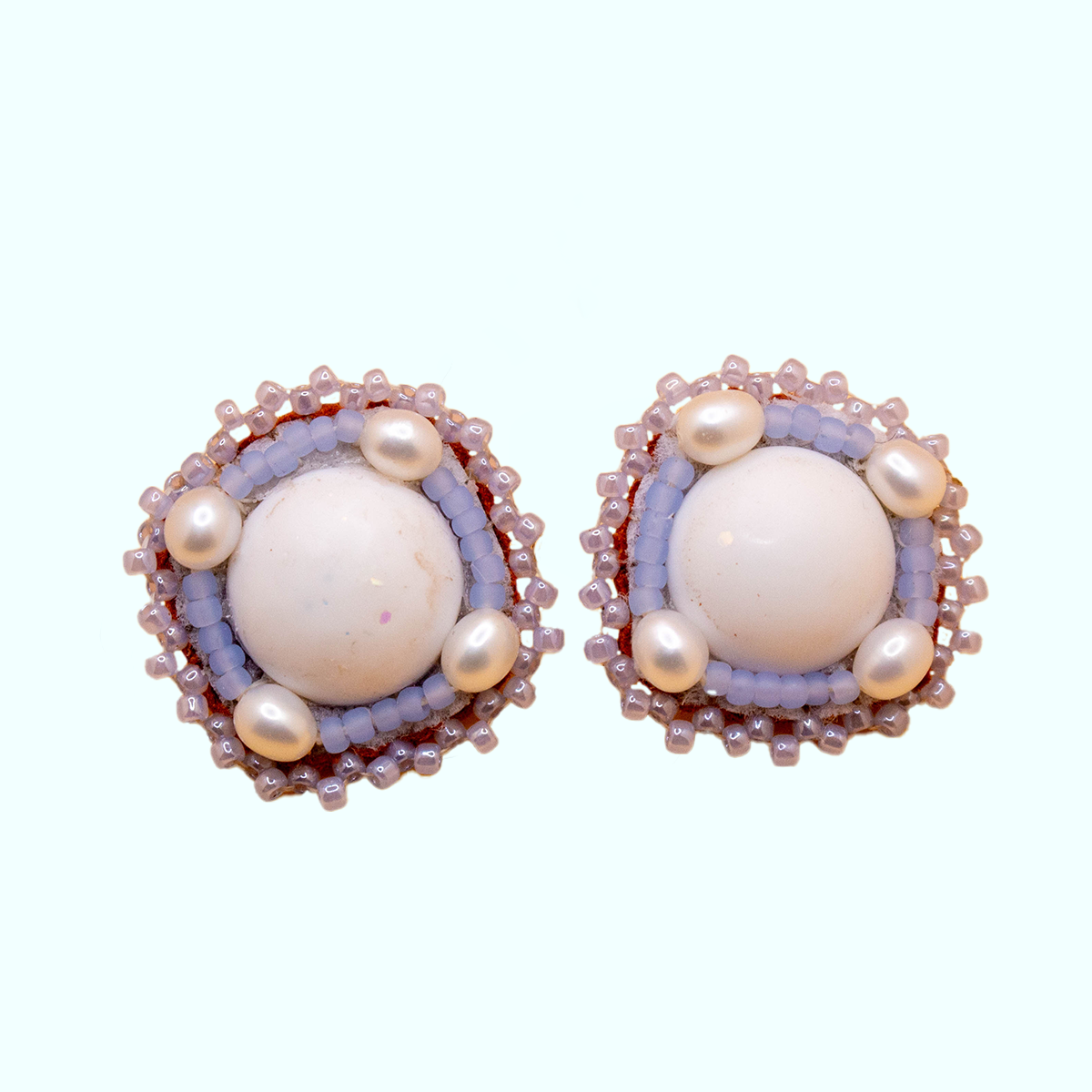 Front view of handmade beaded earrings with white resin center, purple beads, and pearls